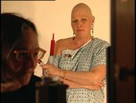 Elsa in the foreground, dimly lit and blurry.  Debbie in focus in the background, holding a syringe containing red liquid.